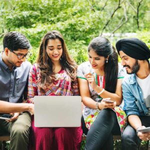 Group of young students sitting outdoors, collaborating on a laptop and tablet during a study session.